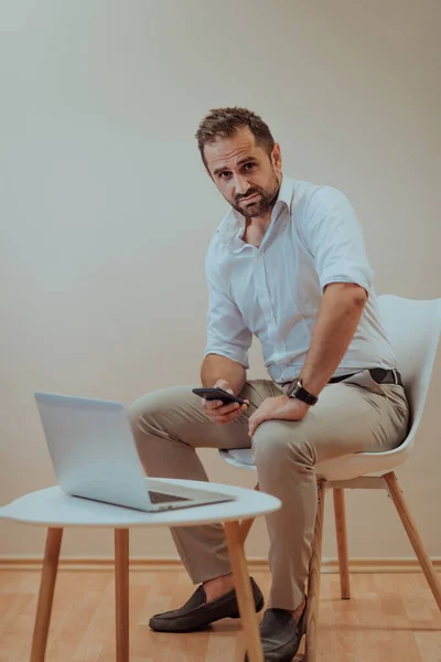 自信のあるビジネスマンは 特定の表情でノートパソコンやスマートフォンを使用し ベージュの背景は 彼の生産性と専門知識を紹介し プロの雰囲気を向上させます — ストック写真