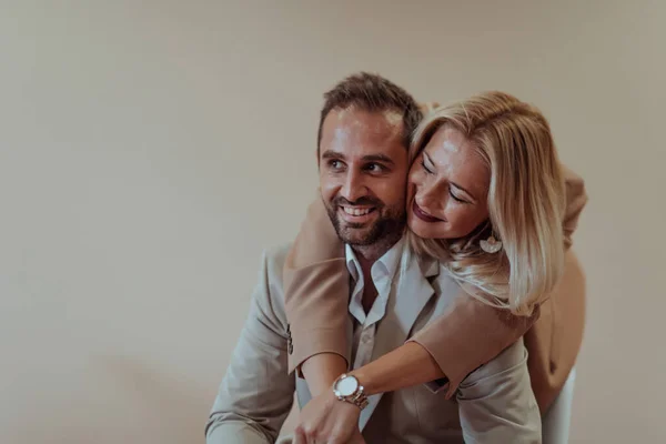 A business couple poses for a photograph together against a beige backdrop, capturing their professional partnership and creating a timeless image of unity and success