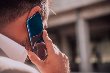 Akıllı telefonunu açık havada kullanan bir işadamı modern profesyonel hayatta teknolojinin ve hareketliliğin kusursuz bütünlüğünü sergiliyor.
