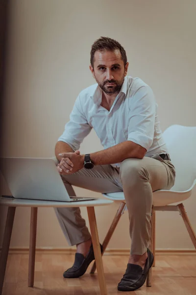 自信のあるビジネスマンは 特定の表情でラップトップを使用して座って ベージュの背景は 彼の生産性と専門知識を紹介し プロの雰囲気を向上させます — ストック写真