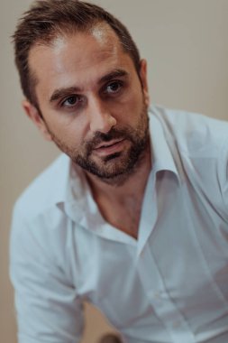 Kendinden emin bir işadamı otururken, bej bir arka plan profesyonel atmosferi geliştirir, üretkenliğini ve uzmanlığını gösterir.