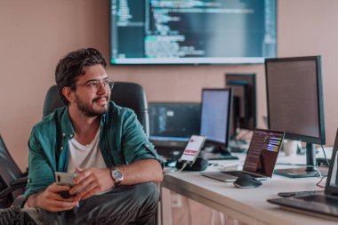 Bir programcı ofisinde otururken akıllı telefon uygulamalarını özenle test ediyor. Yüksek kalite fotoğraf