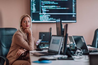 Bilgisayarlarla çevrili bir programcı ofisinde oturan bir iş kadını uzmanlığını ve teknolojiye olan bağlılığını gösteriyor.