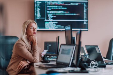 Bilgisayarlarla çevrili bir programcı ofisinde oturan bir iş kadını uzmanlığını ve teknolojiye olan bağlılığını gösteriyor.