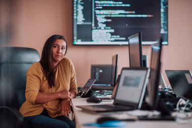 Bilgisayarlarla çevrili bir programcı ofisinde oturan bir iş kadını uzmanlığını ve teknolojiye olan bağlılığını gösteriyor.