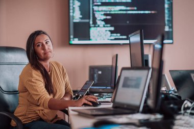 Bilgisayarlarla çevrili bir programcı ofisinde oturan bir iş kadını uzmanlığını ve teknolojiye olan bağlılığını gösteriyor.