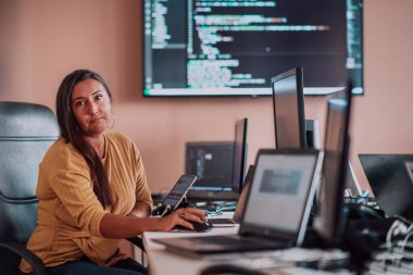 Bilgisayarlarla çevrili bir programcı ofisinde oturan bir iş kadını uzmanlığını ve teknolojiye olan bağlılığını gösteriyor.
