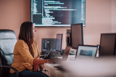 Bilgisayarlarla çevrili bir programcı ofisinde oturan bir iş kadını uzmanlığını ve teknolojiye olan bağlılığını gösteriyor.