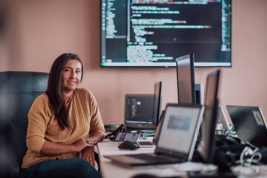 Bilgisayarlarla çevrili bir programcı ofisinde oturan bir iş kadını uzmanlığını ve teknolojiye olan bağlılığını gösteriyor.