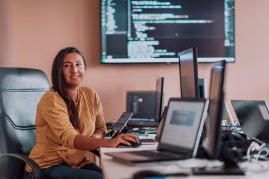 Bilgisayarlarla çevrili bir programcı ofisinde oturan bir iş kadını uzmanlığını ve teknolojiye olan bağlılığını gösteriyor.