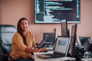 Bilgisayarlarla çevrili bir programcı ofisinde oturan bir iş kadını uzmanlığını ve teknolojiye olan bağlılığını gösteriyor.