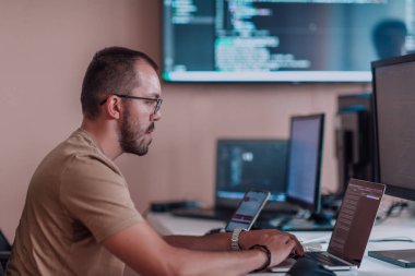 Bir programcı ofisinde otururken akıllı telefon uygulamalarını özenle test ediyor. Yüksek kalite fotoğraf