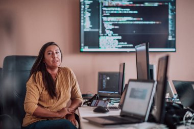 Bilgisayarlarla çevrili bir programcı ofisinde oturan bir iş kadını uzmanlığını ve teknolojiye olan bağlılığını gösteriyor.
