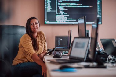 Bilgisayarlarla çevrili bir programcı ofisinde oturan bir iş kadını uzmanlığını ve teknolojiye olan bağlılığını gösteriyor.