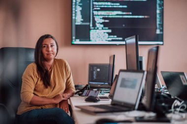 Bilgisayarlarla çevrili bir programcı ofisinde oturan bir iş kadını uzmanlığını ve teknolojiye olan bağlılığını gösteriyor.