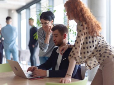 Modern bir ofis ortamında dizüstü bilgisayardaki verileri incelerken iki bayan meslektaşıyla satış istatistikleri hakkında tartışan bir işadamı.. 