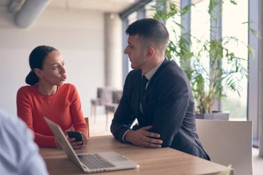 Genç bir girişimci çift, büyük ve modern bir ofiste birlikte oturur ve dizüstü bilgisayarlarındaki istatistikleri ve verileri analiz ederler..