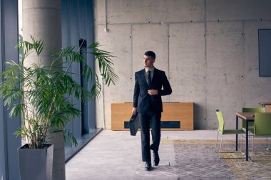 Evrak çantası olan kendine güvenen bir işadamı modern bir ofiste karizma ve kararlılık yayarak başarıyı ve profesyonel mükemmelliği sembolize eder.