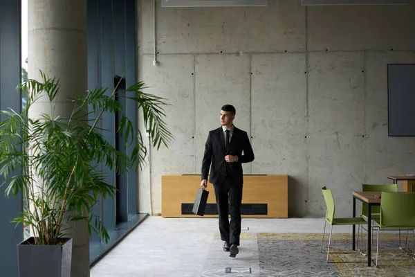 一位自信的商人 带着公文包大步走过现代化的办公室 流露出非凡的魅力和决心 象征着成功和卓越的专业水平 — 图库照片