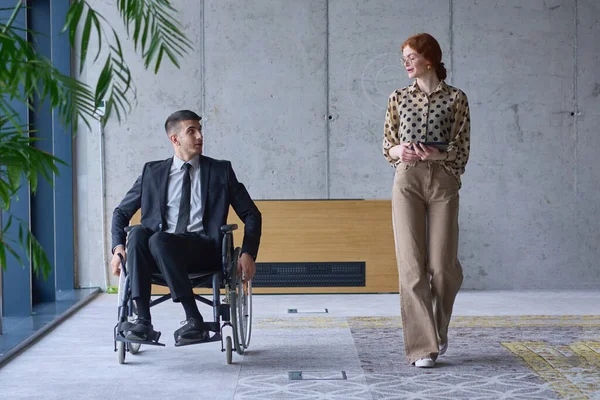 一个坐在轮椅上的商人和他的女同事一起坐在一个现代化的办公室里 代表了团队合作 包容和支持的力量 营造了一个充满活力和包容的工作环境 — 图库照片