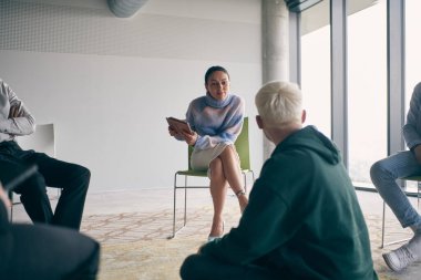 Çemberin merkezinde oturan genç bir işadamı, iş fikirlerini meslektaşlarıyla tutkuyla paylaşıyor, dinamik ve çekici bir işbirliği ve yenilik atmosferini teşvik ediyor.