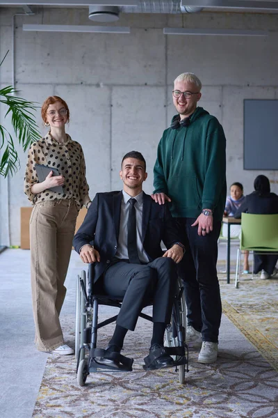 坐在轮椅上的残疾商人被现代办公室的同事们围绕着 展示了面对挑战时团队合作 包容和赋权的力量 — 图库照片