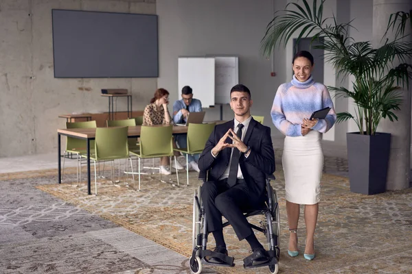 チームワーク インクルージョン サポートの力を表し ダイナミックで包括的な労働環境を育成し 現代のオフィスで一緒に車椅子や彼の女性の同僚のビジネスマン — ストック写真