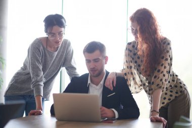 Modern bir ofis ortamında dizüstü bilgisayardaki verileri incelerken iki bayan meslektaşıyla satış istatistikleri hakkında tartışan bir işadamı.. 