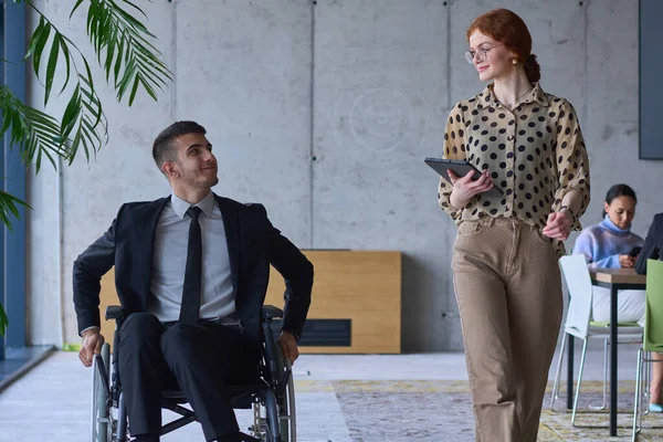 一个坐在轮椅上的商人和他的女同事一起坐在一个现代化的办公室里 代表了团队合作 包容和支持的力量 营造了一个充满活力和包容的工作环境 — 图库照片