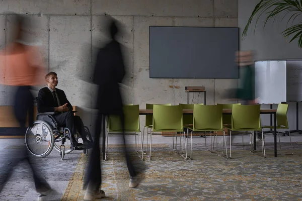 彼らはワークスペースを移動すると 彼らのサポートと連帯を象徴し ぼやけた動きで描かれている彼の同僚に囲まれた近代的なオフィスの車椅子のビジネスマン — ストック写真