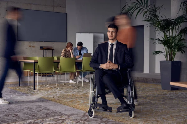 彼らはワークスペースを移動すると 彼らのサポートと連帯を象徴し ぼやけた動きで描かれている彼の同僚に囲まれた近代的なオフィスの車椅子のビジネスマン — ストック写真