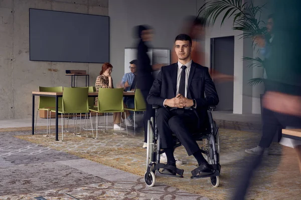 一位坐在现代办公室轮椅上的商人在同事们的簇拥着下 他们的动作模糊不清 象征着他们在工作空间中的支持和团结 — 图库照片