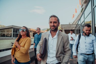 Çeşitli iş adamları ve meslektaşları iş yerlerinin yanından birlikte yürüyorlar, şirkette işbirliği ve takım çalışması sergiliyorlar.