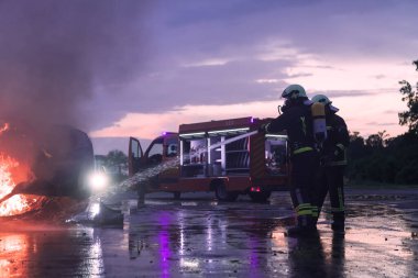 İtfaiyeciler yangın söndürücüyü araba kazasında alevle savaşmak için kullanıyorlar. Geceleyin itfaiyeci endüstriyel ve kamu güvenliği konsepti kurtarma. Yüksek kalite fotoğraf