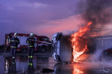 İtfaiyeciler yangın söndürücüyü araba kazasında alevle savaşmak için kullanıyorlar. Geceleyin itfaiyeci endüstriyel ve kamu güvenliği konsepti kurtarma. Yüksek kalite fotoğraf