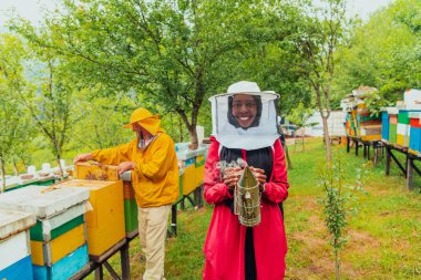 Portrait of a Muslim African American woman in the beekeeping department of a honey farm holding a jar of honey in her hand. 