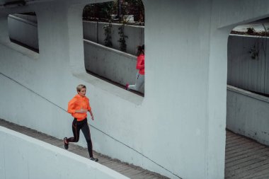 Modern bir şehir ortamında koşan spor elbiseli iki kadın. Sportif ve sağlıklı yaşam tarzı kavramı. 