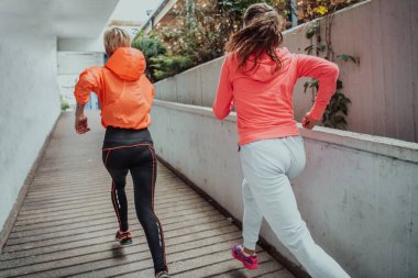 Modern bir şehir ortamında koşan spor elbiseli iki kadın. Sportif ve sağlıklı yaşam tarzı kavramı. 