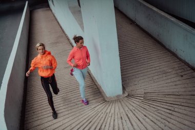 Modern bir şehir ortamında koşan spor elbiseli iki kadın. Sportif ve sağlıklı yaşam tarzı kavramı. 