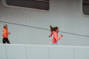 Modern bir şehir ortamında koşan spor elbiseli iki kadın. Sportif ve sağlıklı yaşam tarzı kavramı. 