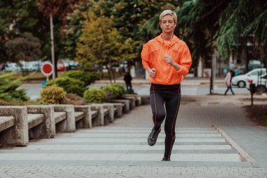  A blonde in a sports outfit is running around the city in an urban environment. The hot blonde maintains a healthy lifestyle