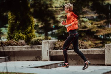  Spor kıyafetli bir sarışın şehirde şehir içinde koşuşturuyor. Seksi sarışının sağlıklı bir yaşam tarzı var.