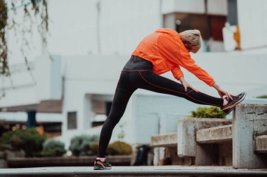 Spor giyim sektöründe çekici bir kadın yaz aylarında yeşilliklerin arasında yaya yolunda koşmadan önce bir bacağını esnetiyor. Antrenman, spor, aktivite, fitness, tatil ve eğitim eşdeğer
