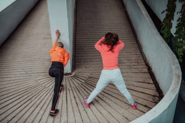 Two women warming up together and preparing for a morning run in an urban environment. Selective focus . 