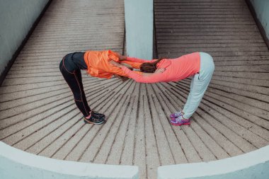 Two women warming up together and preparing for a morning run in an urban environment. Selective focus . 