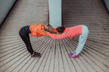 Two women warming up together and preparing for a morning run in an urban environment. Selective focus . 