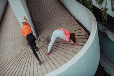 Two women warming up together and preparing for a morning run in an urban environment. Selective focus . 