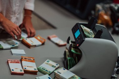 Banka çalışanları banka kasasında kağıt banknotları sıralarken ve sayarken para sayma makinesi kullanıyorlar. Bankada büyük miktarda para var.. 