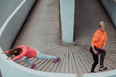 Two women warming up together and preparing for a morning run in an urban environment. Selective focus . 