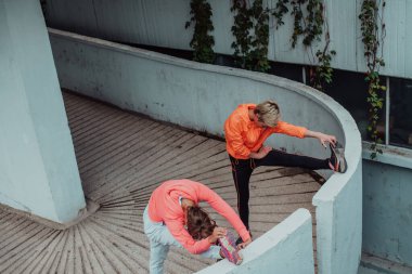 Two women warming up together and preparing for a morning run in an urban environment. Selective focus . 